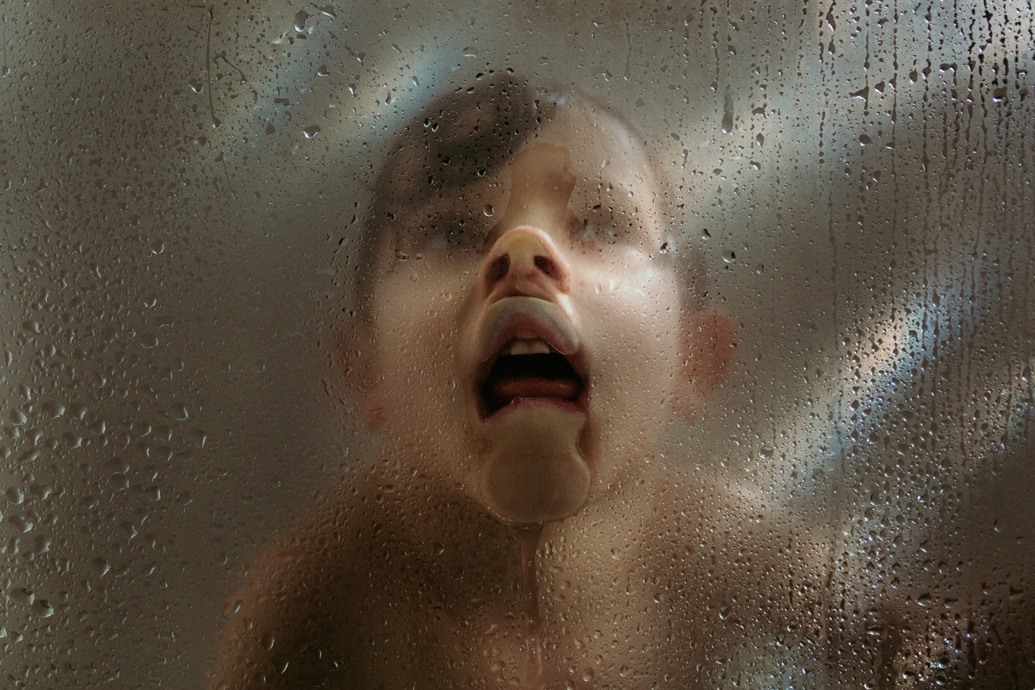 A photo of a young boy with his face pressed up agains the steamy glass in the shower making a funny face.